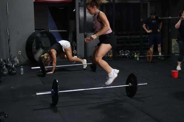 Athletes doing burpees over the bar in class