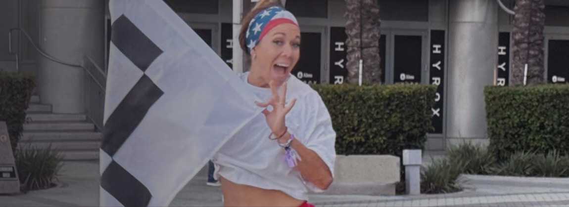Jaci Caceres celebrando con la bandera de meta afuera de una sede HYROX