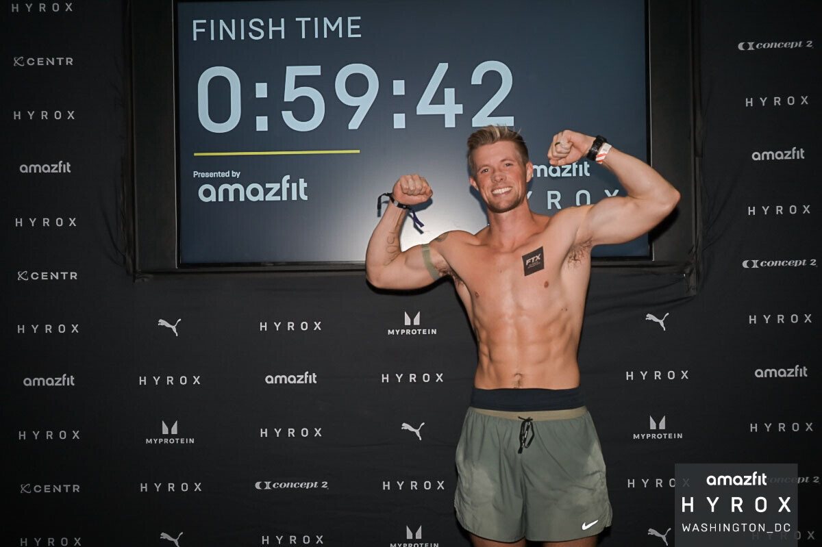 Coach Clayton Marshall in front of the HYROX Washington DC finish clock showing 0:59:42